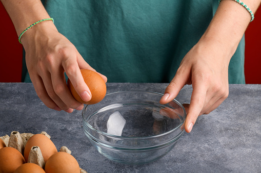 A woman's hand cracking an egg into a clear glass bowl in the gray kitchen table, the process of cooking, Lifestyle, close up