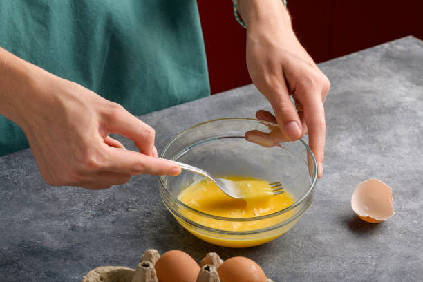 istock Female hands beat eggs with fork in a glass bowl on a gray kitchen table 2078353866