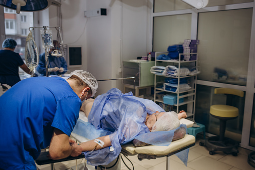 Physician with sterile protective clothing and face mask monitors a patient in the intensive care unit.