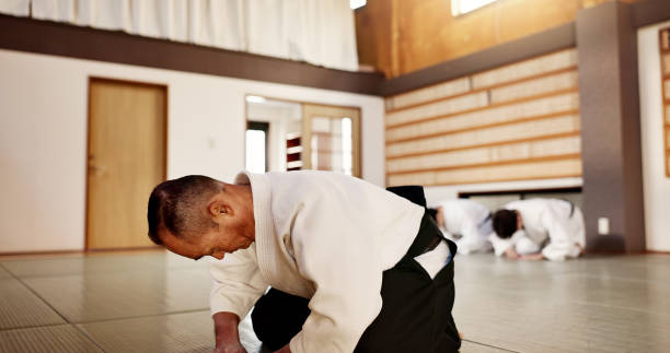 istock Aikido class, sensei and students with bow, martial arts or respect for calm at training, gym or dojo. Japanese people, floor and club for exercise, workout and fitness with fight, ready and battle 2078356148