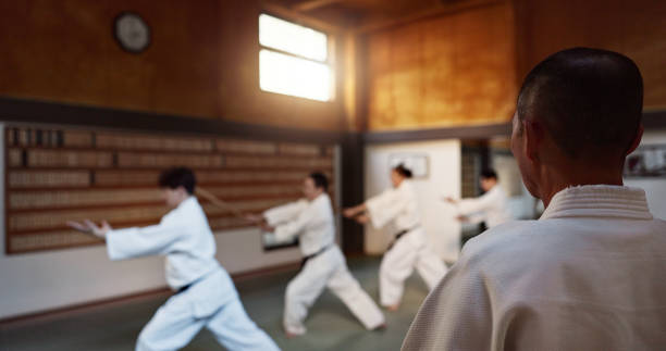 Aikido, group and class with sensei, weapon training and wooden sword for self defence exercise. Dojo, students and athlete in a gym or studio with fight challenge, black belt practice and fitness