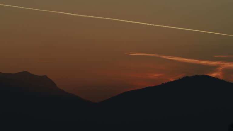 Timelapse of the Sun Setting Behind a Mountain Symbolizing the End of Fasting for Muslims During Ramadan. The Plane is Leaving a White Trail in the Sky