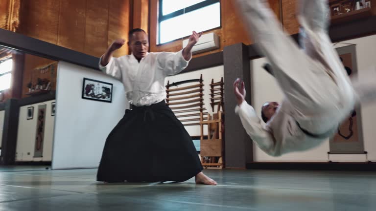 Aikido, master and fight with a sensei in martial arts with student of self defence, discipline and training. Demonstration, class or Japanese man with black belt in fighting with education of skill