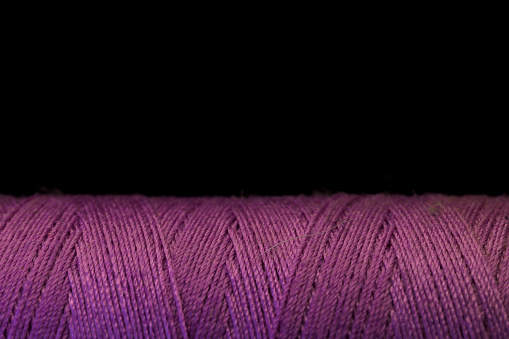 Spool of purple thread for sewing with black background horizontally with copy space