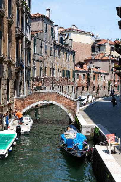Venice, Veneto - Italy - 06-09-2021: Gondola and motorboats moored along a peaceful narrow Venetian canal