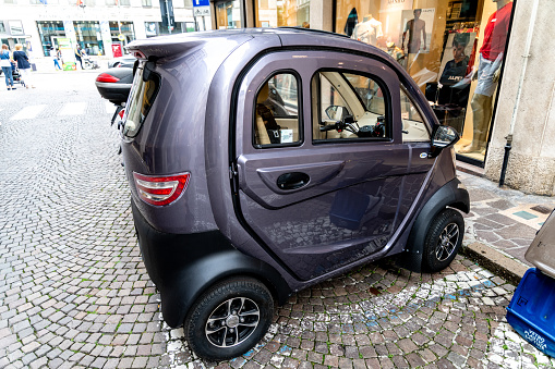 Venice, Veneto - Italy - 06-10-2021: Small purple electric car parked on a motorcycle parking space in a cobblestone street in a city