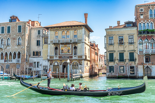 Venice, Veneto - Italy - 06-10-2021: A gondola cruises by a mosaic-adorned Venetian palazzo on a sunny day
