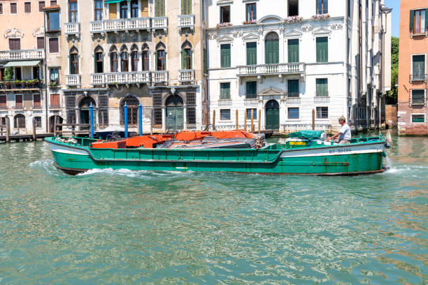 Venice, Veneto - Italy - 06-10-2021: A green cargo boat makes its way through a canal in Venice, past historical facades