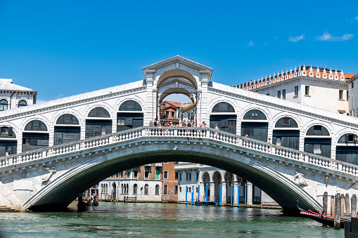 Venice, Veneto - Italy - 06-10-2021: Iconic Rialto Bridge arching over Venice's Grand Canal against a clear blue sky
