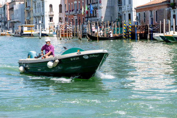 Venice, Veneto - Italy - 06-10-2021: A lone man pilots a small motorboat on the vibrant canals of Venice, passing by gondolas
