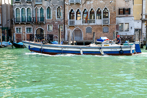 Venice, Veneto - Italy - 06-10-2021: A workboat cruises by, loaded with goods against aged Venetian facades