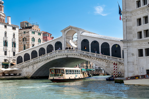 Venice, Veneto - Italy - 06-10-2021: Veniceâs iconic Rialto Bridge frames a passing vaporetto on the bustling Grand Canal