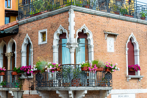 Venice, Veneto - Italy - 06-10-2021: Ornate Gothic windows and balcony of a Venetian building, adorned with vibrant flowers