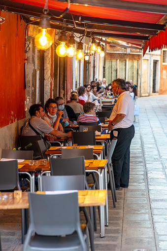 Venice, Veneto - Italy - 06-10-2021: Diners enjoy meals at an outdoor restaurant along a narrow Venetian street
