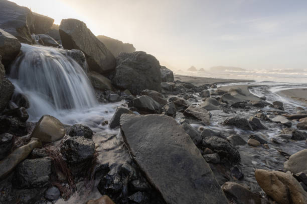 A rocky shoreline with a stream of water flowing through it. The water is clear and the rocks are large and jagged. The scene is peaceful and serene