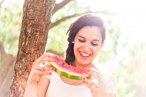 Smiling young caucasian woman at park on a hot summer day - Woman eating a refreshing slice of watermelon - Summer and lifestyle concepts.