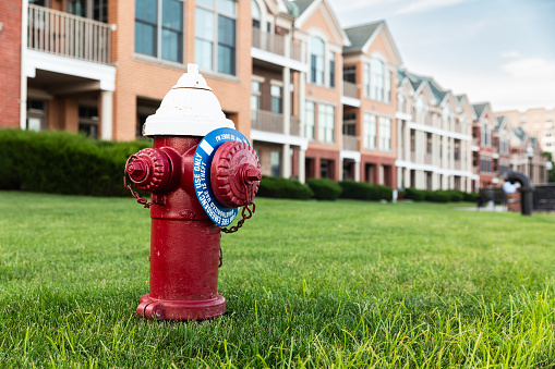 Vibrant red fire hydrant stands before residential townhouses with green lawn in New Jersey - Red fire hydrant in suburban neighborhood
