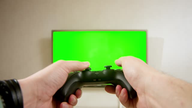 Close-up of a gamer's hands playing a competitive video game on a green chromatic TV screen.