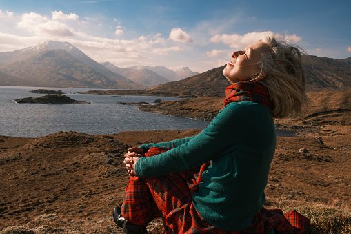 Senior woman wearing a traditional red tartan kilt enjoying the wonderful scenery at Loch Quoich in the Highlands of Scotland.