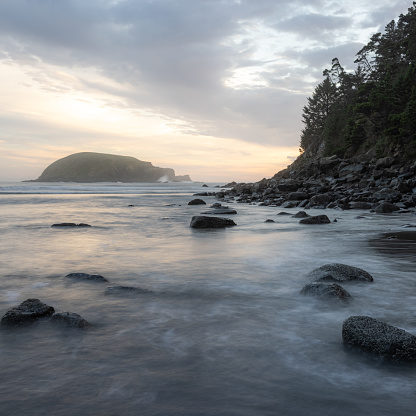 The ocean is calm and the sky is cloudy. The rocks on the shore are scattered and the water is still