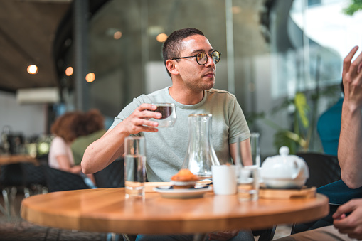 Spending quality time together, Hispanic and Caucasian male friends gather at a table in a modern cafe. With cups of artisan coffee before them, they engage in animated discussions, creating an atmosphere of connection and shared enjoyment as they make the most of their time together.