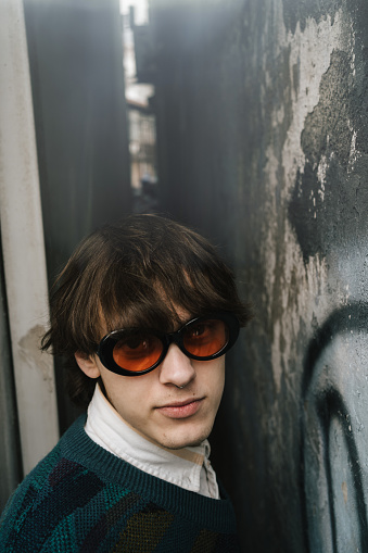 Young man with retro vibe stands in narrow alley, his vintage sunglasses reflecting soul of urban environment around him.