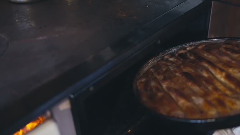 Woman's Hand Takes Baked Traditional Bosnian Borek from the Hot Stove with a Cloth. The burek can be filled with savory ingredients like potato, meat, or cheese, wrapped in thin layers of filo dough