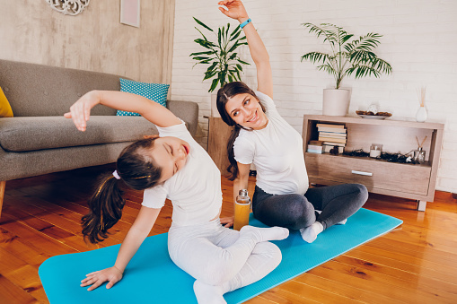 Happy pregnant mother exercising yoga with her daughter.