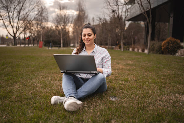 istock Woman outdoors sitting on grass working on laptop 2078567777