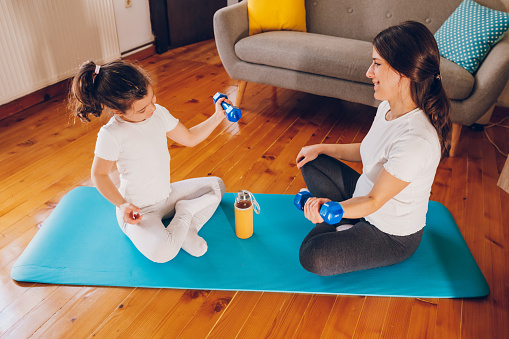 Happy pregnant mother doing exercise with her daughter.