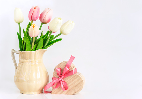 bouquet of wihte and pink tulips and heart shape gift box with pink bow on a white background with space for text
