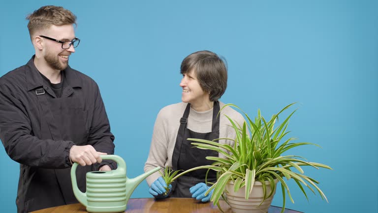 Man and woman watering potted plant on blue background