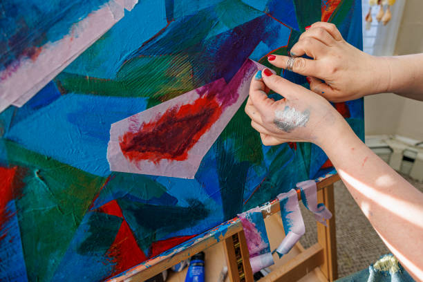 Woman, a painter is working on her art abstract painting, using masking tape to isolate areas on the canvas.