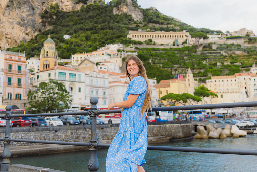 Side view of smiling female tourist with long hair exploring Amalfi Coast and walking the authentic streets with colourful houses by the sea