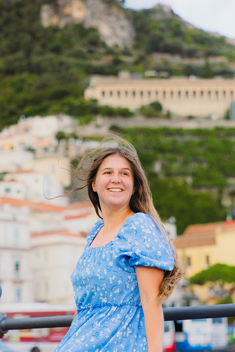 Portrait of smiling female tourist with long hair exploring Amalfi Coast and walking the authentic streets with colourful houses by the sea