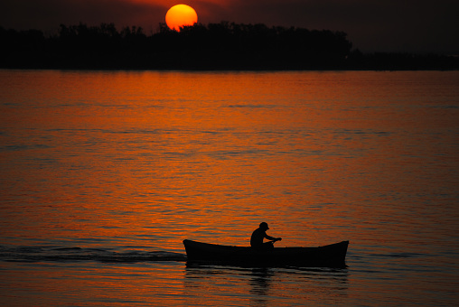 Fisherman in his canoe crossing the river in a sunset