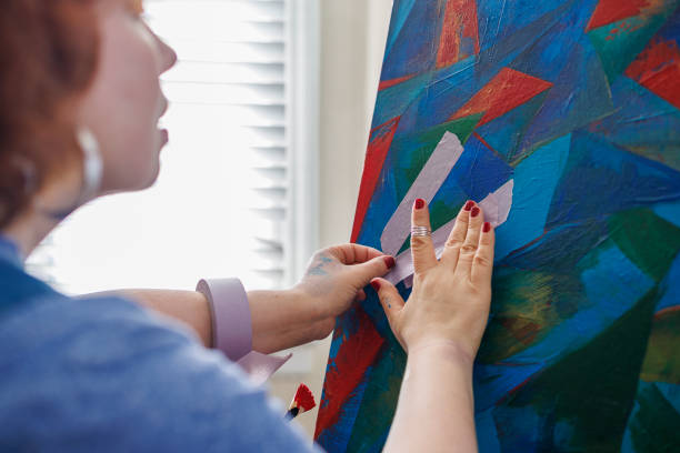 istock Masking tape application on the art canvas. A woman, a painter, is using painter tape when she is working on the painting in her studio 2078637773