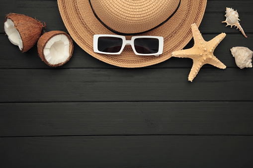 Summer accessories with coconuts on black wooden background. Space for text