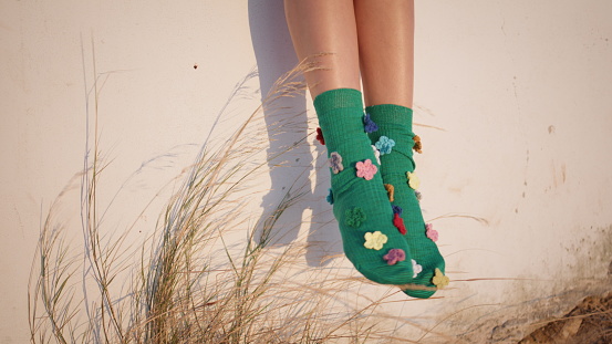 Legs wearing colorful socks in sunlight outdoors. Carefree kid enjoying evening vacation. Unrecognized happy girl teenager rest in summer. Funny creative accessory with flowers. Style fashion concept