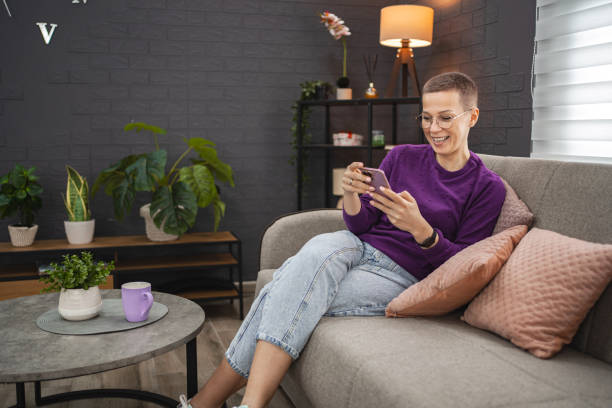 istock Smiling Caucasian woman with short hair using mobile phone while relaxing at home 2078672214