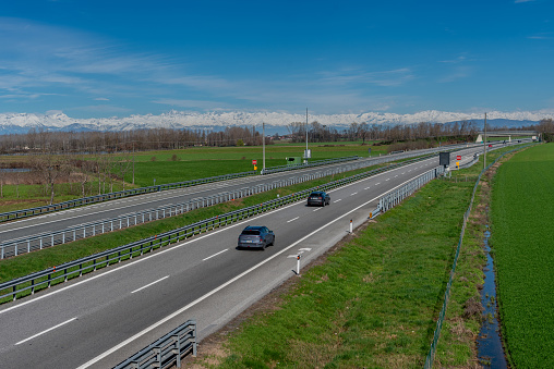 The Italian highway crosses the Po Valley countryside near Turin with a view of the snow-capped Cozie Alps in the background