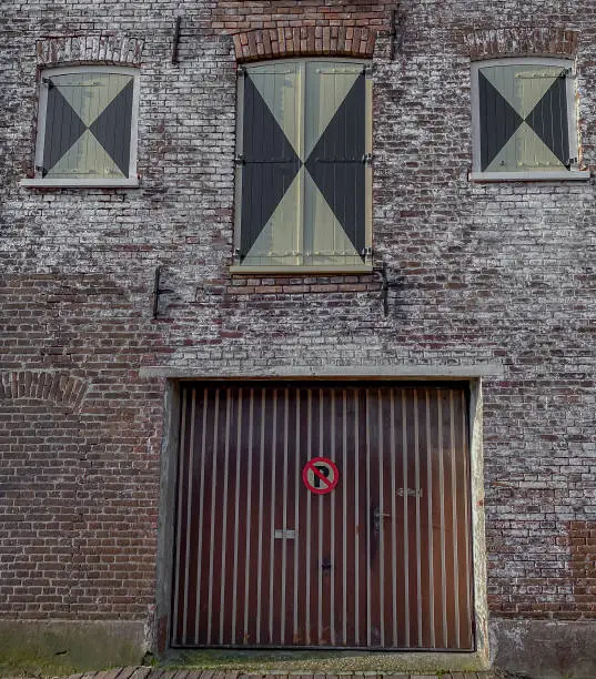 An old brick house with three windows and a sign on the wall that says "Parking is prohibited."