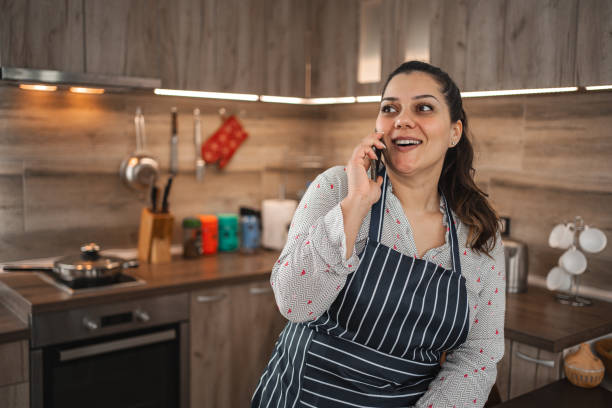 istock Smiling woman talking on the phone while cooking in the kitchen 2078693145