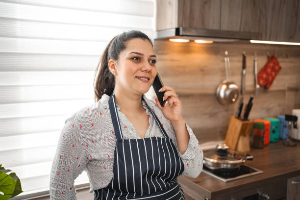istock Smiling woman talking on the phone while cooking in the kitchen 2078693664