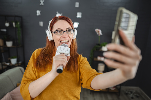 Red haired woman having fun singing with microphone at home.