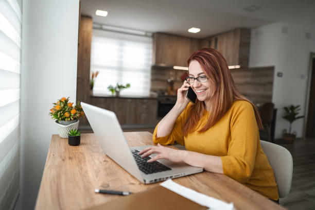 istock Red haired Caucasian woman talking on a phone call while working on laptop at home 2078696423