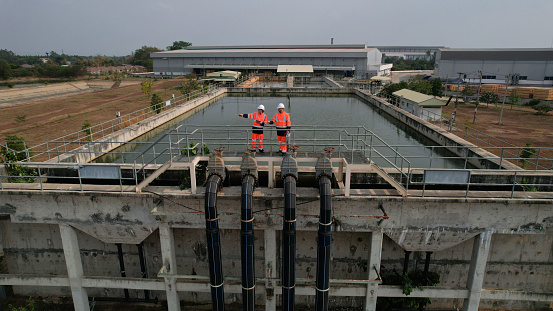 Aerial view shot of two diverse environmentalists Working on the sunlight at a wastewater treatment plant in the industrial estate by walking around and checking the quality of the water