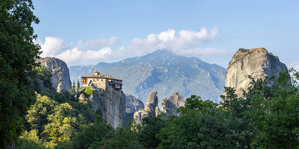 Panoramic view of the monastery in Meteora in the morning summer light with mountains in the background.