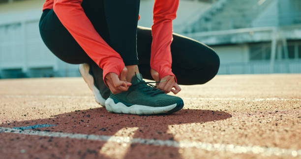 closeup of young asian female athlete runner tying shoelaces in preparation for running exercise getting ready for jogging outdoors. healthy workout exercise. - running track women running spring stock-fotos und bilder