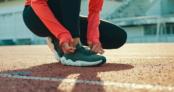 Closeup of young Asian female athlete runner tying shoelaces in preparation for running exercise getting ready for jogging outdoors. Healthy workout exercise concept.